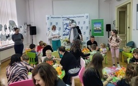 Postać w kostiumie zajączka stoi pomiędzy uczestnikami warsztatów