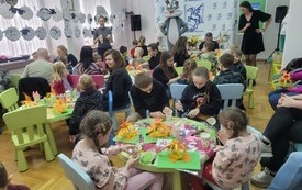 Dzieci wraz z opiekunami siedzą przy stolikach i tworzą prace plastyczne