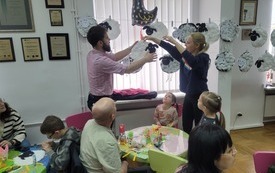 Opiekunowie tworzą girlandę z papierowych baranków