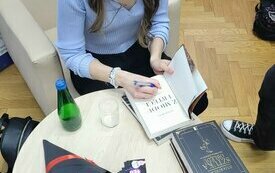 Autorka siedzi przy stoliku i podpisuje swoje książki