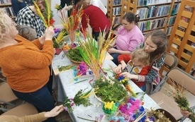 Stół z kolorowymi kwiatami, trawami i bukszpanem służącymi do wyrobu palm