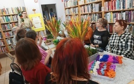 Grupa osób siedzi przy stolikach w bibliotece