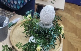 Dekoracja z kwiatów i pisanki na drewnianej tacy.