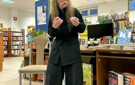 Starszy mężczyzna z długimi włosami, w tle regały z książkami.