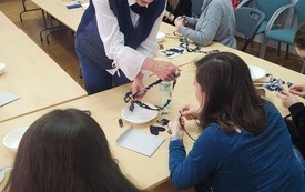 Kobieta w okularach pokazuje w jaki sposób wykonać naszyjnik