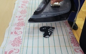 Na ściereczce serce z materiału, nad nim osoba trzymająca w ręku żelazko.