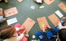 Dzieci siedzą na dywanie i wykonują prace plastyczne o tematyce wielkanocnej