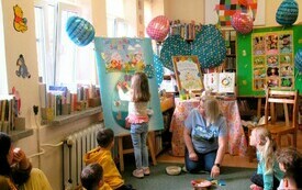 Dzieci siedzą na dywanie przy tablicy z wielkim papierowym jajkiem