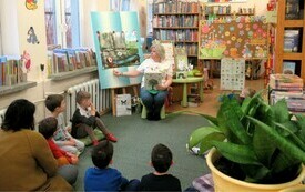 Dzieci siedzą na dywanie w bibliotece i oglądają prezentację przygotowaną przez bibliotekarkę