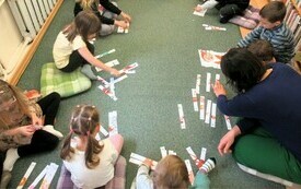 Dzieci siedzą na dywanie i układają obrazki z kolorowych pasków papieru