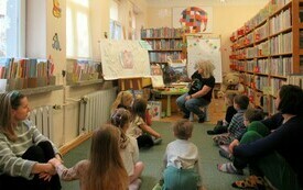 Grupa dzieci z rodzicami siedzi na dywanie w bibliotece