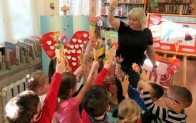 Bibliotekarka stoi z bukietem papierowych kwiatów, wokół niej dzieci