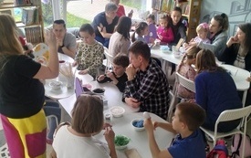 Wielkanocne warsztaty grupowe dla rodziców i dzieci, którzy tworzą ozdoby przy stolikach.