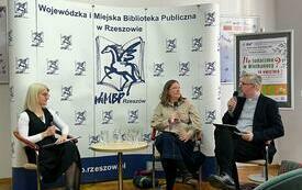 Przy stoliku dwie kobiety i mężczyzna. W tle baner z logiem biblioteki.