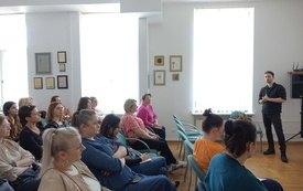 Na krzesłach siedzą bibliotekarze i słuchają prowadzącego. 