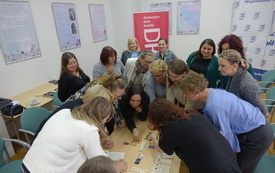 Uczestnicy szkolenia pochylają się nad stołem z grą planszową