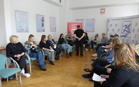 Widok sali szkoleniowej, prowadzący stoi na środku pomiędzy uczestnikami