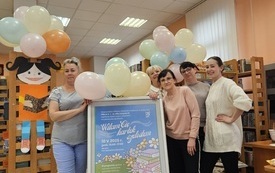 Pięć kobiet na zdjęciu z plakatem wydarzenia. W tle kolorowe balony i regały z książkami.