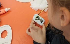 Dziewczynka malująca pędzelkiem drzewko na kamieniu.