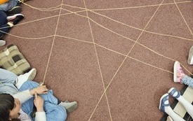 Dzieci siedzące w kółku tworzące linie z włóczki.