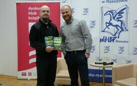Gość spotkania pozuje do wspólnego zdjęcia z mężczyzną trzymającym w ręku książki.