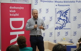 Mężczyzna z mikrofonem, w tle banery DKK i WiMBP w Rzeszowie