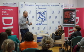 Gość spotkania mówi do zebranej publiczności siedzącej na krzesełkach.