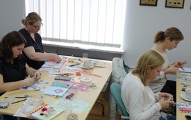 Na stole wyłożone materiały papiernicze. Bibliotekarki wyklejają notatnik.