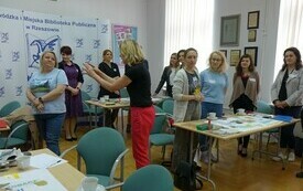 Uczestnicy szkolenia stoją przy stolikach. 