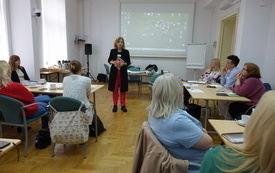 Kobieta pośrodku sali z książką w ręku przemawia do zebranych.