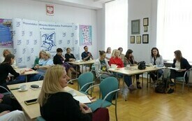 Przy dużych stołach siedzą bibliotekarze.