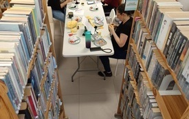 Grupa osób uczestniczących w warsztatach siedzi przy stoliku pośród regałów z książkami