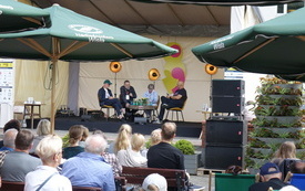 Na scenie pod namiotem siedzi cztery osoby i rozmawia. Przed nimi publiczność.