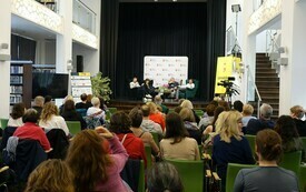 Na scenie cztery osoby siedzące w fotelach. Przed sceną zgromadzona publiczność.