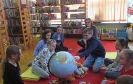 Grupa dzieci siedzących na dywanie wok&oacute;ł dużego globusa