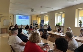 Uczestnicy seminarium siedzą przy stołach zwr&oacute;ceni w kierunku ekranu projekcyjnego na kt&oacute;rym wyświetlana jest prezentacja 