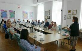 Kobieta w marynarce przemawia do uczestników siedzących przy stołach.