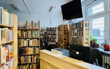 Lada biblioteczna, nad nią wiszący telewizor, w tle regały z książkami