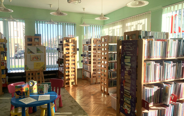 Przeszklone pomieszczenie z regałami z książkami i kolorowym stolikiem