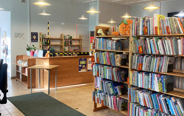 Pomieszczenie z ladą biblioteczną i regałami z książkami oświetlone lampami sufitowymi