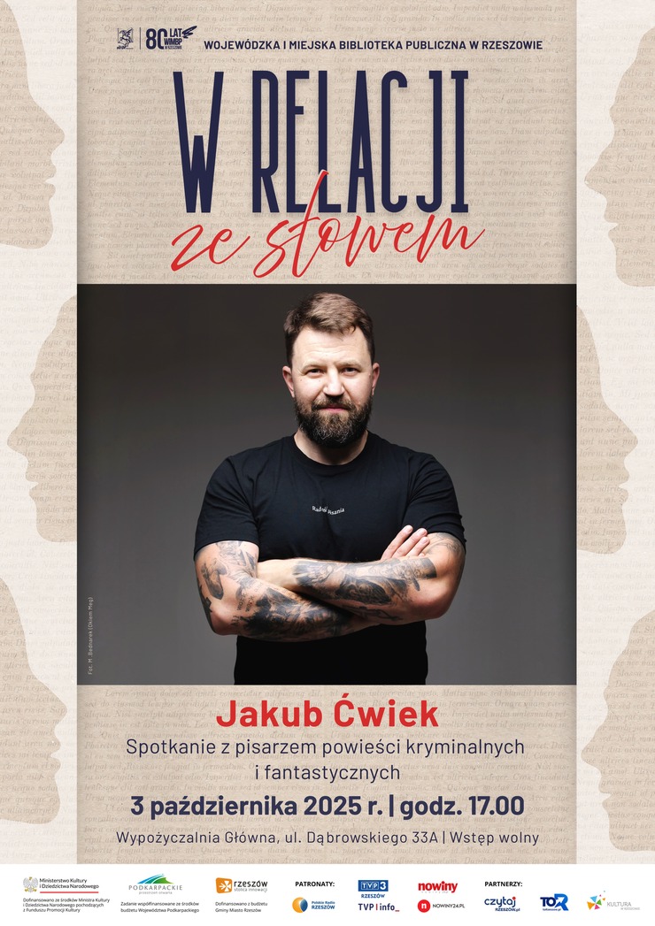 Mężczyzna z brodą i tatuażami na rękach stoi z założonymi rękami.
