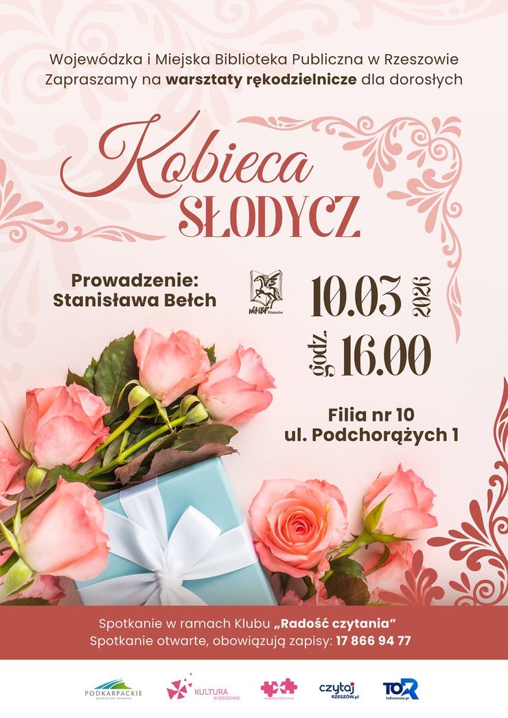Pudełko prezentowe z&nbsp;kokardą, obok kwiaty r&oacute;ż.
